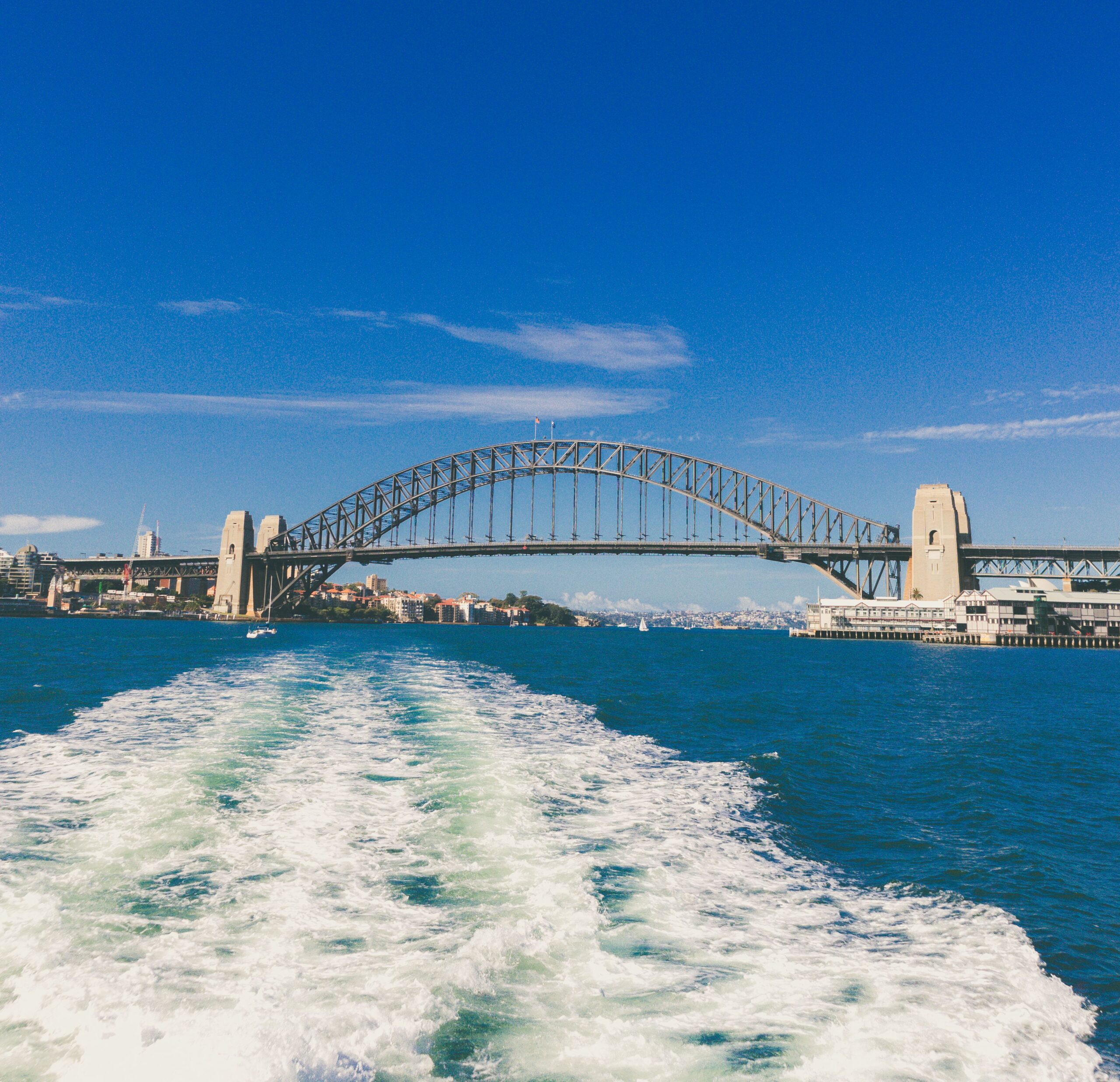 View of Sydney Harbour Bridge under a clear blue sky with the wake of a boat in the foreground.