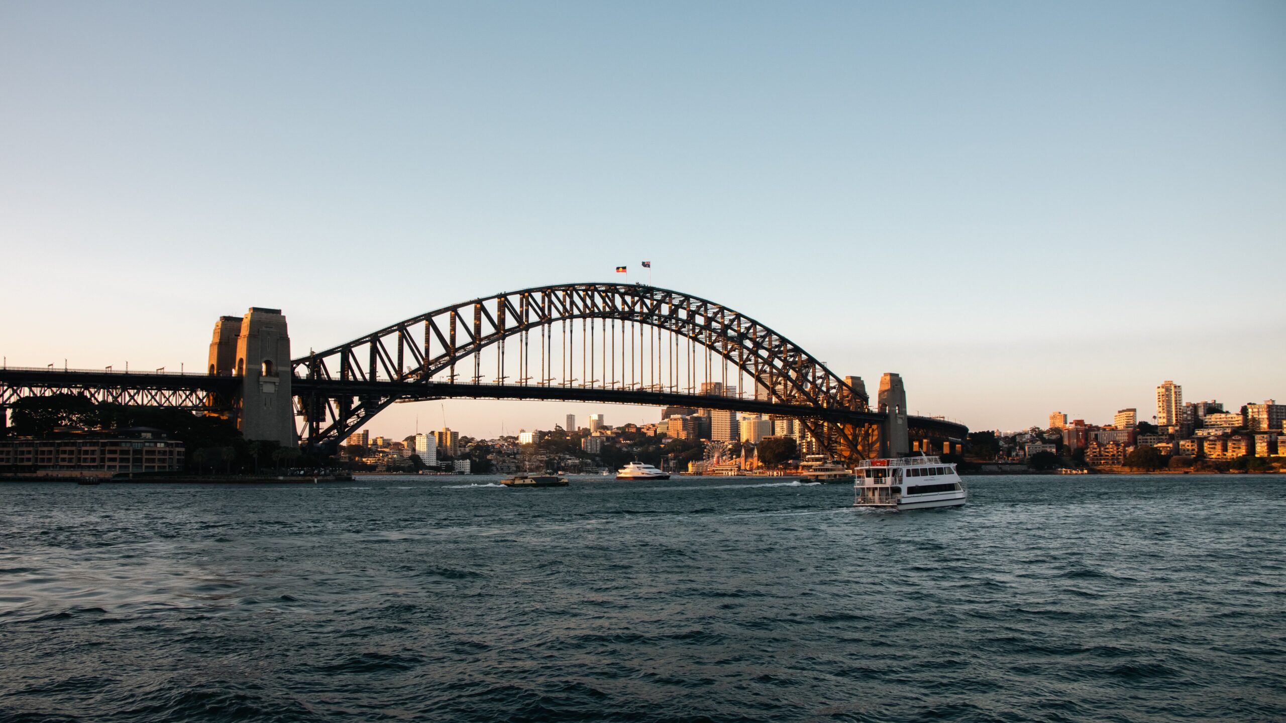 Sydney Harbour Bridge at sunset with ferry and city skyline in the background.